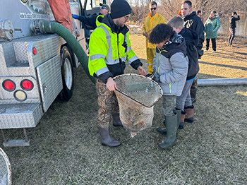 People gathered to watch and assist stocking at Spring Mill Pond at Island Lake Recreation Area (Livingston County).