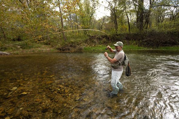 A fly fisherman stands in the middle of a stream working his fly rod in the air.