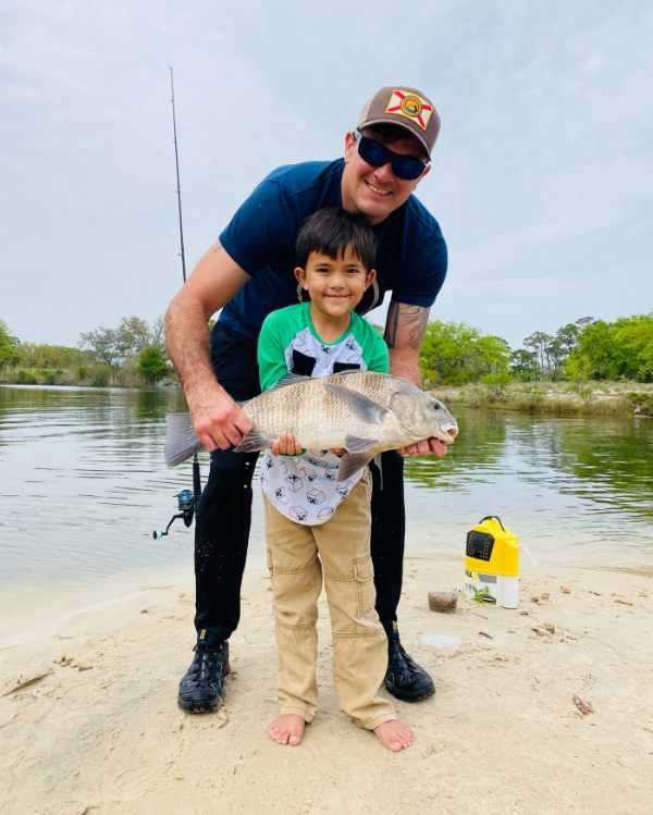 Adult and child holding a blackdrum in front of shoreline