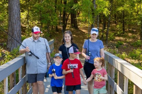 People on wooded trail walking with fishing poles in hand