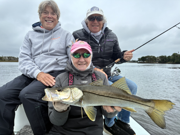 Three adults on motor vessel holding a snook