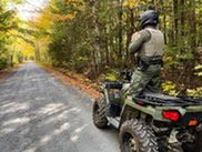 Maine game warden in green uniform patrolling on an ATV with fall foliage background