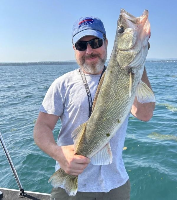 Angler standing in boat on water holding up a walleye
