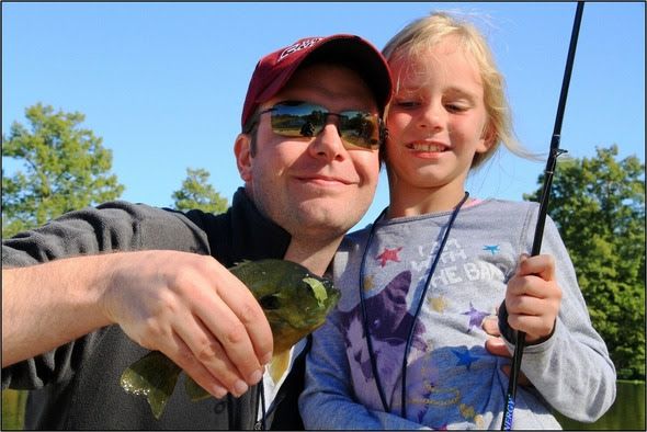 A father poses with his young daughter as he holds up a fish they just caught.